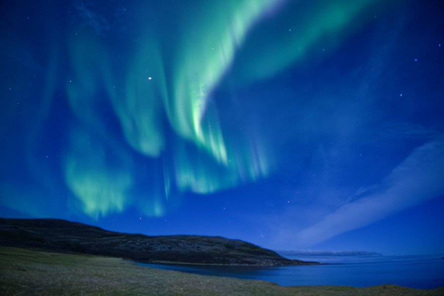 Nordlicht über der Küstenlandschaft bei Tromsø – grüne und violette Lichtschleier am klaren Nachthimmel.