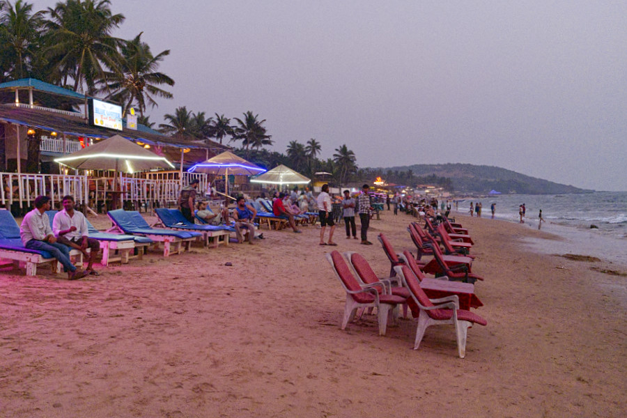 Abendstimmung am Strand von Anjuna mit Liegestühlen, Strandbars und Spaziergängern am Wasser.